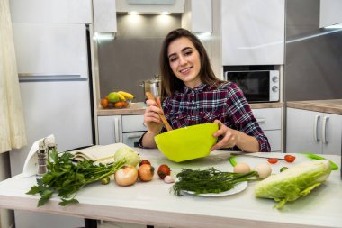 Mutfak masasında poz veren kız sağlıklı bir yaşam için farklı sebze ve sebzelerden oluşan bir salata hazırlıyor.