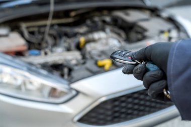 Otomotiv tamircisi arka planda araba ve kaputu açık halde anahtarları elinde tutuyor. Onarım