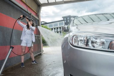 Ukraynalı ince kadın arabasını su püskürtüsüyle temizleyip yıkıyor. araba yıkama