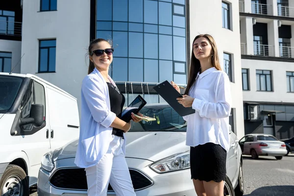 Rent or car buy concept. Two women with dollar bundle posing near car