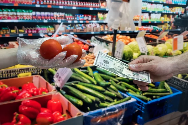 seller in gloves sells fresh vegetables. man gives dollars for groceries in the supermarket. covid19