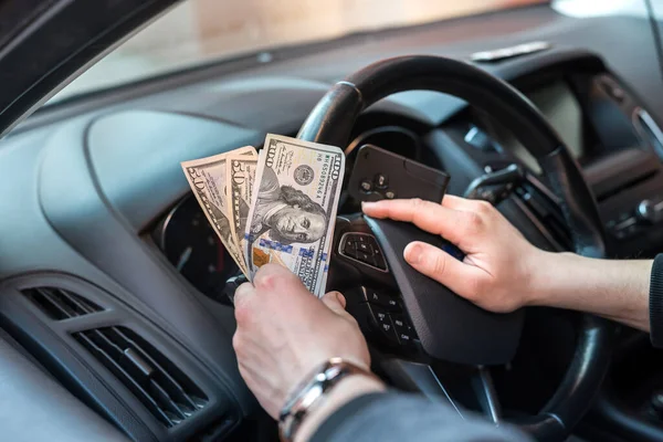 dollar and car key in male\'s hand inside car. pay in goods or rent car