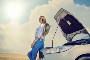 Stresli genç bir kadın arabasının motoruna bakıyor. Yolculuk sorunları. Arabanın tamire ihtiyacı var..