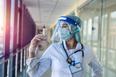 Üniformalı güzel hemşire ve yüz kalkanı elinde şırıngayla klinikte aşı bekliyor.