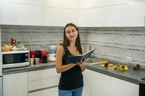 beautiful young woman reads a notebook in the kitchen to cook healthy food for breakfast.