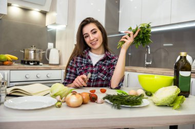 Mutfak masasında poz veren kız sağlıklı bir yaşam için farklı sebze ve sebzelerden oluşan bir salata hazırlıyor.