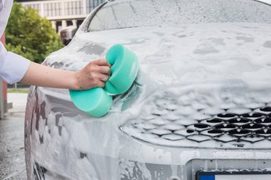 Yeşil süngerli ve köpüklü kadın elleri arabasını yıkıyor. Temizlik kavramı.