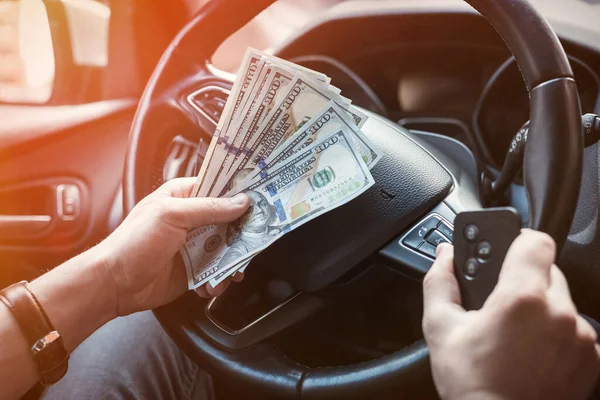dollar and car key in male\'s hand inside car. pay in goods or rent car