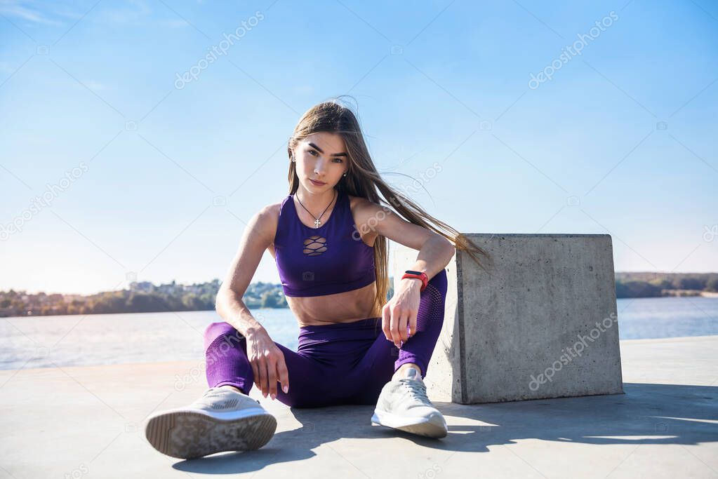 girl in sports uniform resting after morning exercises on the shore of the lake. health and beauty concept