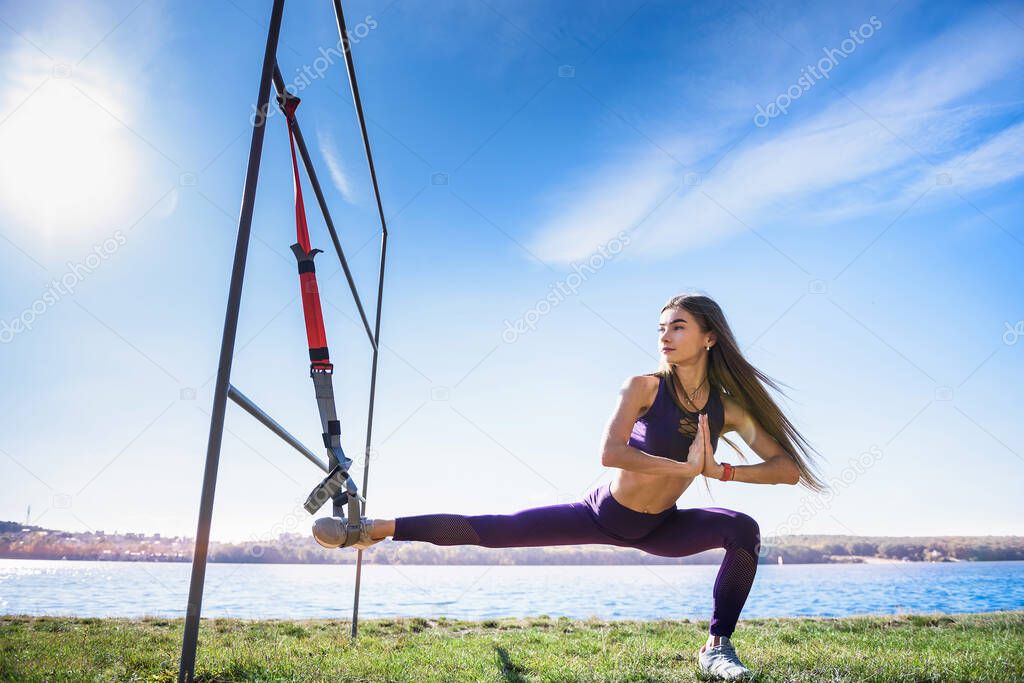 young female athlete  doing morning  exercises  training  with trx fitness straps in the park. Concept of healthy workout and lifestyle