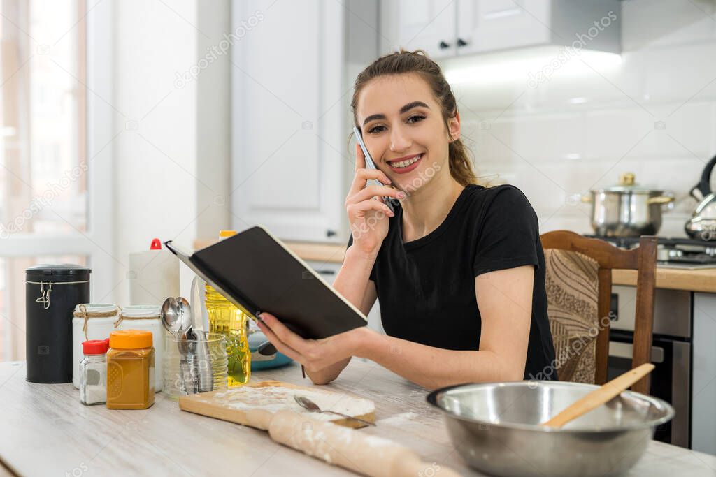 Young woman cooking cake with flour, reading notepad recipe in kitchen table. Healthy food