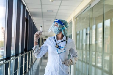 Üniformalı güzel hemşire ve yüz kalkanı elinde şırıngayla klinikte aşı bekliyor.