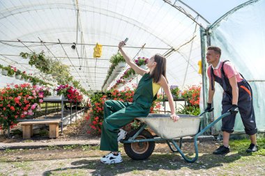 Genç mutlu çift serada eğlenirken erkekler ortak bir iş aldıktan sonra karısını el arabasıyla gezdiriyorlar.