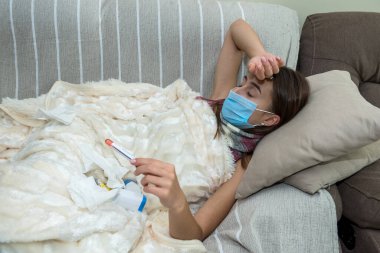 Hasta kadın kanepede yatar ve koronavirüsün pozitif sonuçlarına bakar.