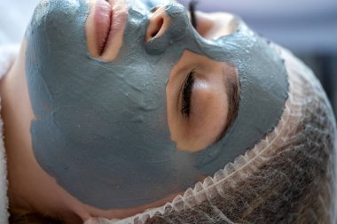 Güzellik kliniğindeki bir yatakta yüz maskesi takan genç bir kadın. Sağlık hizmeti kavramı