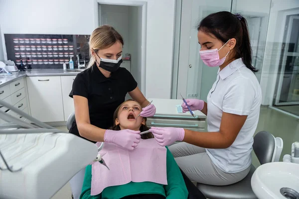 Female dentist and young assistant doing repairing patient tooth in dental ambulant. Doctor practice