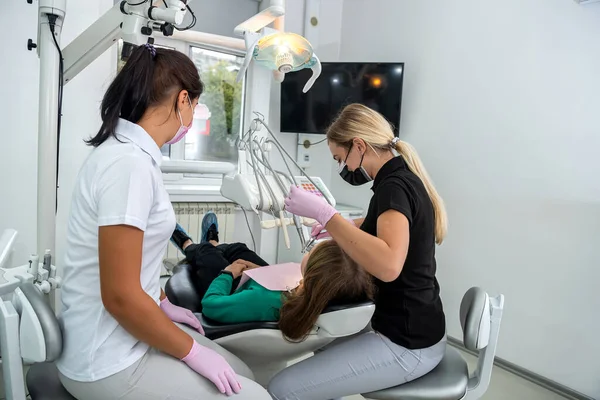 Female dentist and young assistant doing repairing patient tooth in dental ambulant. Doctor practice