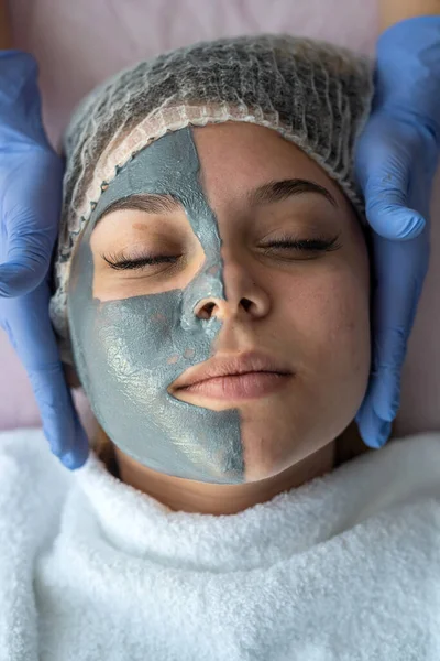 hands of beautician applying beauty mask on young woman face at wellness beauty spa. healthcare