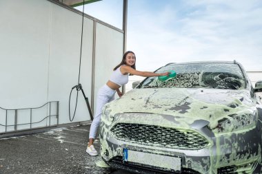 El yıkama servisindeki güzel kadın sürücü. Oto pisliğini temizlemek için sünger beyaz köpük kullan.