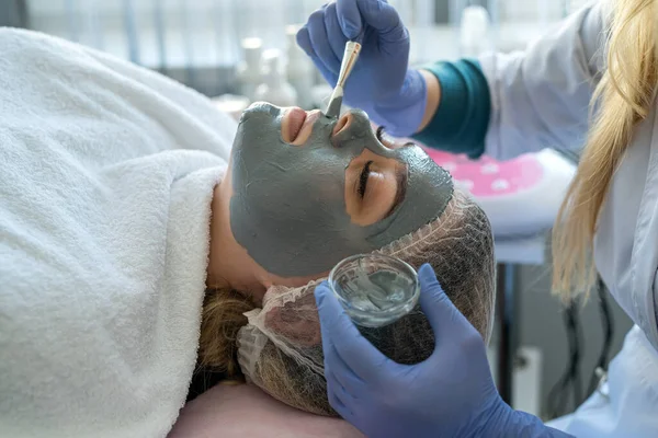 hands of beautician applying beauty mask on young woman face at wellness beauty spa. healthcare