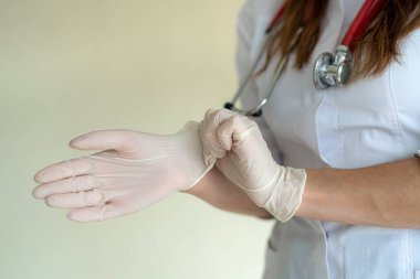 Kadın doktor, klinikte sıkı çalışma gününden önce koruyucu ameliyat eldivenleri giyer. Covid19 'dan güvenlik