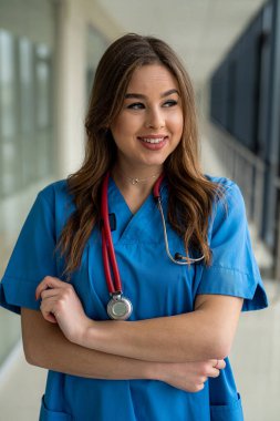 Hastane koridorundaki koronavirüs salgını sırasında mavi üniformalı sevimli bir hemşirenin portresi. Kameraya poz veriyor.