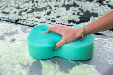 Araba yıkama istasyonunda sabun köpüklü sünger kullanan bir kadın.