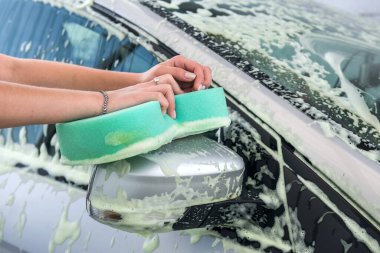 Modern arabasını yıkamak için köpüklü yeşil sünger kullanan yakın plan kadın elleri. 