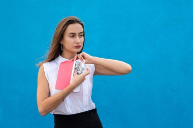 Güzel genç bir iş kadını mavi arka planda dolarlarla dolu bir zarf tutuyor. Yolsuzluk kavramı, maaş veya alışveriş