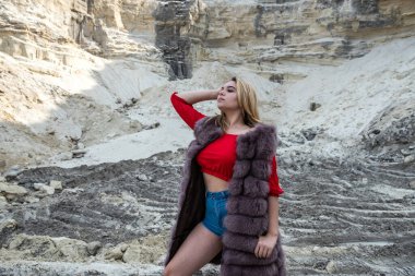 Yaz mevsiminde kum kayalarının yanında poz veren kürklü ve günlük giysili genç bayan portresi.