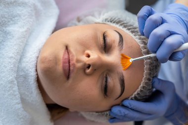 Güzellik uzmanı, genç bir kadın yüz hastasına şifa kremi sürüyor. Tedavi terapisi ve cilt bakımı