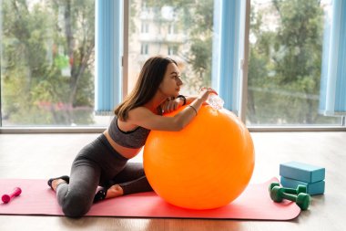 Çekici bir kadın spor salonunun penceresinin yanında fitness egzersizi için spor topu kullanıyor.