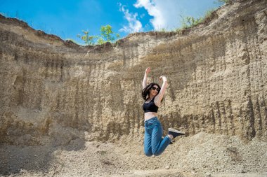 Taş ocağındaki kum kayalarının üzerinde poz veren sıradan giysili sıska bir kız. yaz zamanı