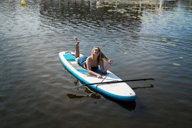 Güzel genç bir kadın sıcak bir yaz gününde SUP tahtasının üzerinde yatıyor. özgürlük