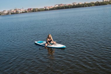 Sıska kız SUP tahtasına uzanmış gevşemiş yazın koyu mavi suda dinleniyor.