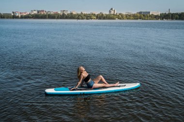 Kürek tahtasında yüzen genç bir kadın, gölet, yaz zamanı
