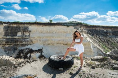 Taş ocağında ya da kanyonda, kayanın yanındaki kumların üzerinde duran sıska genç bir kadın. Mükemmel yolculuğun için yaz zamanı.