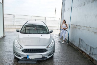 Yüksek basınçlı hortumdan çıkan güzel bir kadın arabasına sabun köpüğü sürüyor. otomatik temizleme konsepti 