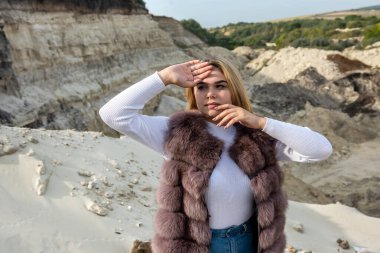 Günlük kıyafet ve kürklü genç bir kadın, açık havada kum kayalarının yanında ateş ediyor. yaz tatili