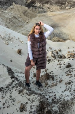 Yaz mevsiminde kum kayalarının yanında poz veren kürklü ve günlük giysili genç bayan portresi.