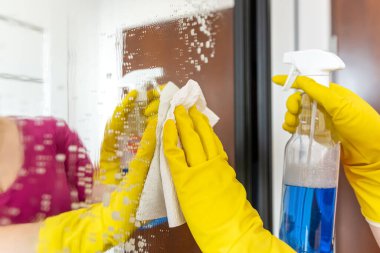 Eldivenli bir kadının elini spreyle yakın plan çek. Gardıroptaki bardağı yıka ve temizle.