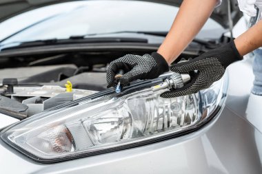 Bir adam arabanın ampulünü değiştiriyor, yolcu arabasının farında lamba tamir ediyor.