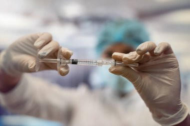 Hemşire portresi beyaz önlük, şapka ve eldiven giyer ve bir hastayı tedavi etmek için bir hastane odasında ilaç enjekte etmeye hazırlanır.