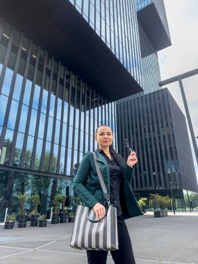 Güzel bir iş kadını çantasıyla modern bina ofisinin yakınında yürüyor.