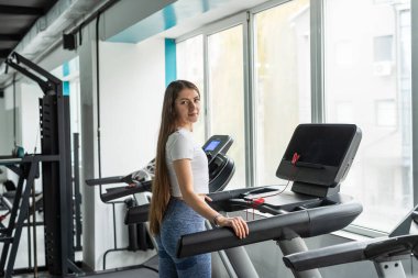 Spor salonunda koşu bandında koşmaya ara veren güzel bir genç kadının portresi. Sağlıklı yaşam için spor salonu