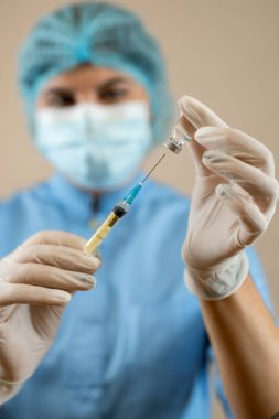 Mavi ceketli bayan doktor, maske ve eldiven aşılı şırınga taşıyor. Sağlık hizmetleri