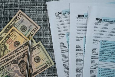 Vergi formları, 100 dolarlık banknotlar ve örülmüş kalemle mali evraklar.