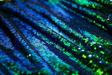 Close-up of shiny blue and green sequin fabric with sparkling texture. Glamorous fabric texture for background, luxury design, or holiday theme. Shallow depth of field, soft focus.