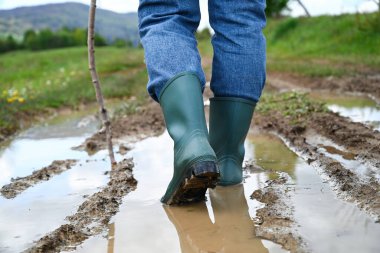 Çamurlu bir su birikintisine adım atan su geçirmez botlar. Mevsimsel açık hava aktivitesi, yağmurlu hava, kırsal yaşam ve doğa yürüyüşü konsepti