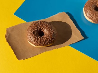 El işi kâğıdı ve renkli geometrik arka plan üzerinde çikolatalı donutun yaratıcı düzeni. Minimalist tatlı konsept. Gıda estetiği. Düzen ya da şablon, metin için alanı kopyala. 